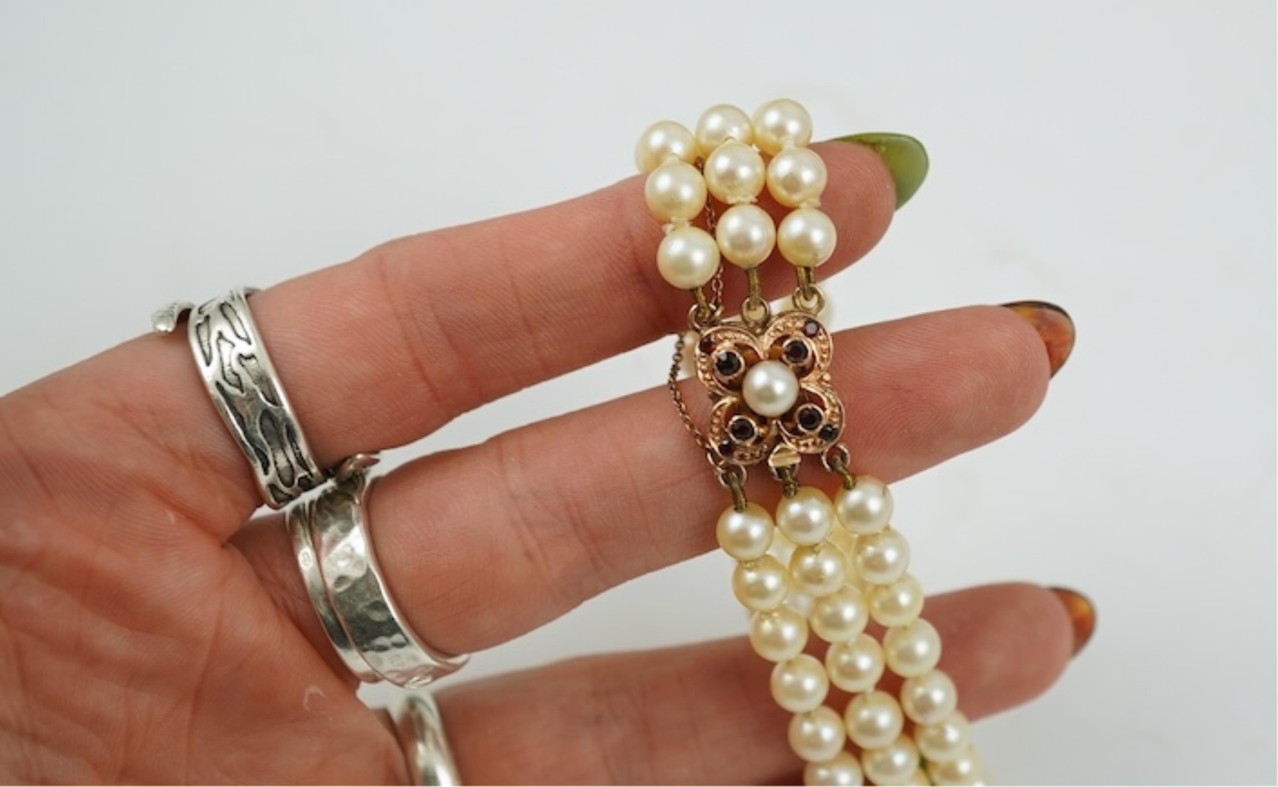 A triple strand cultured pearl bracelet, with a 9ct gold, garnet and cultured pearl cluster set clasp, 16cm.